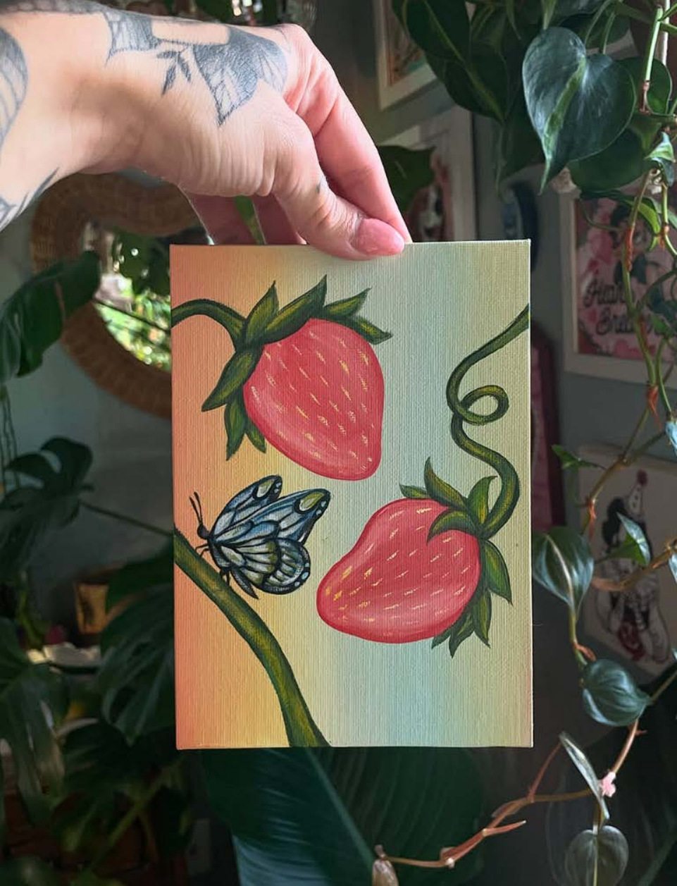 Hand holding a small painting of strawberries and a butterfly