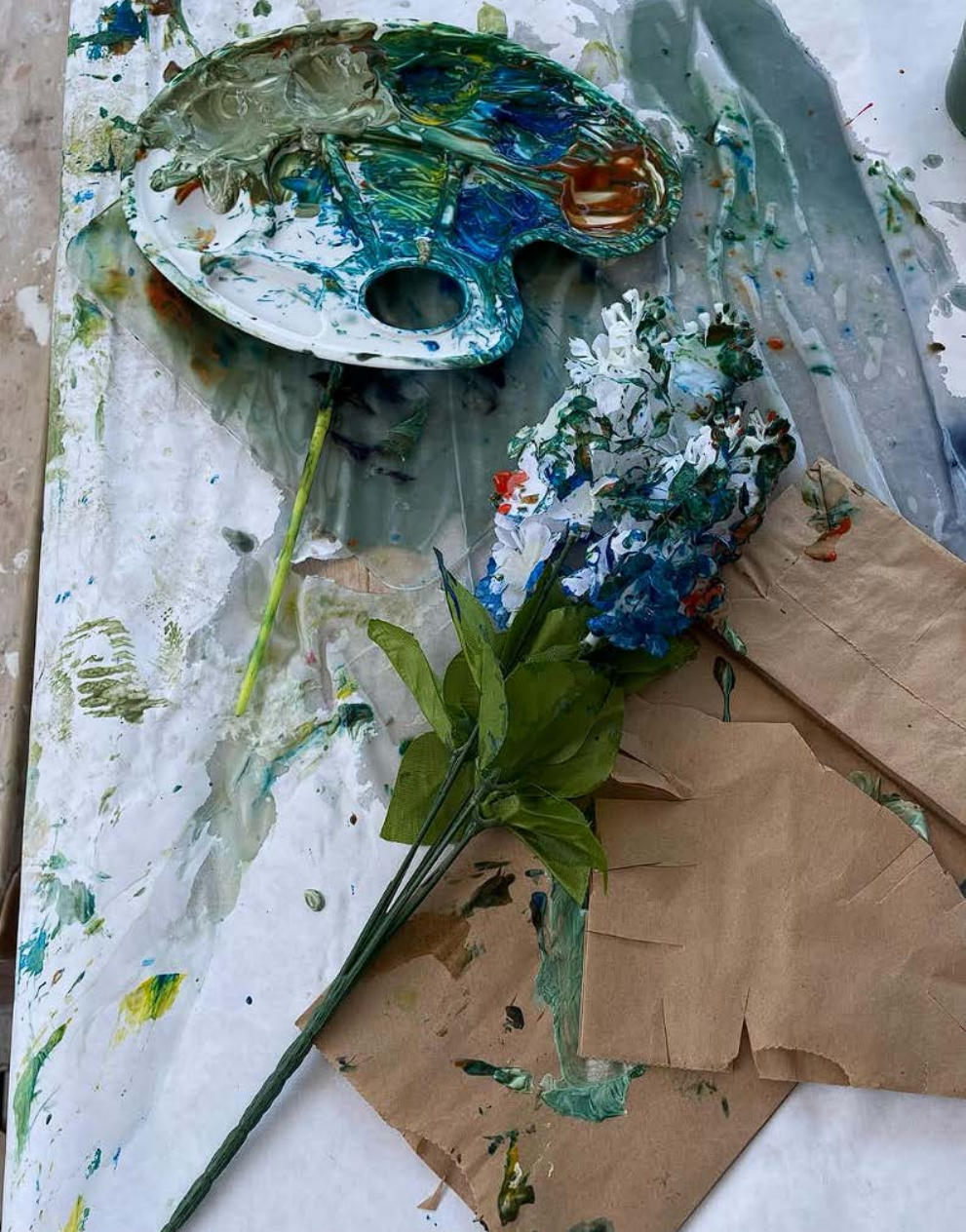 Paint palette, brushes, flowers, and a paint-covered work surface